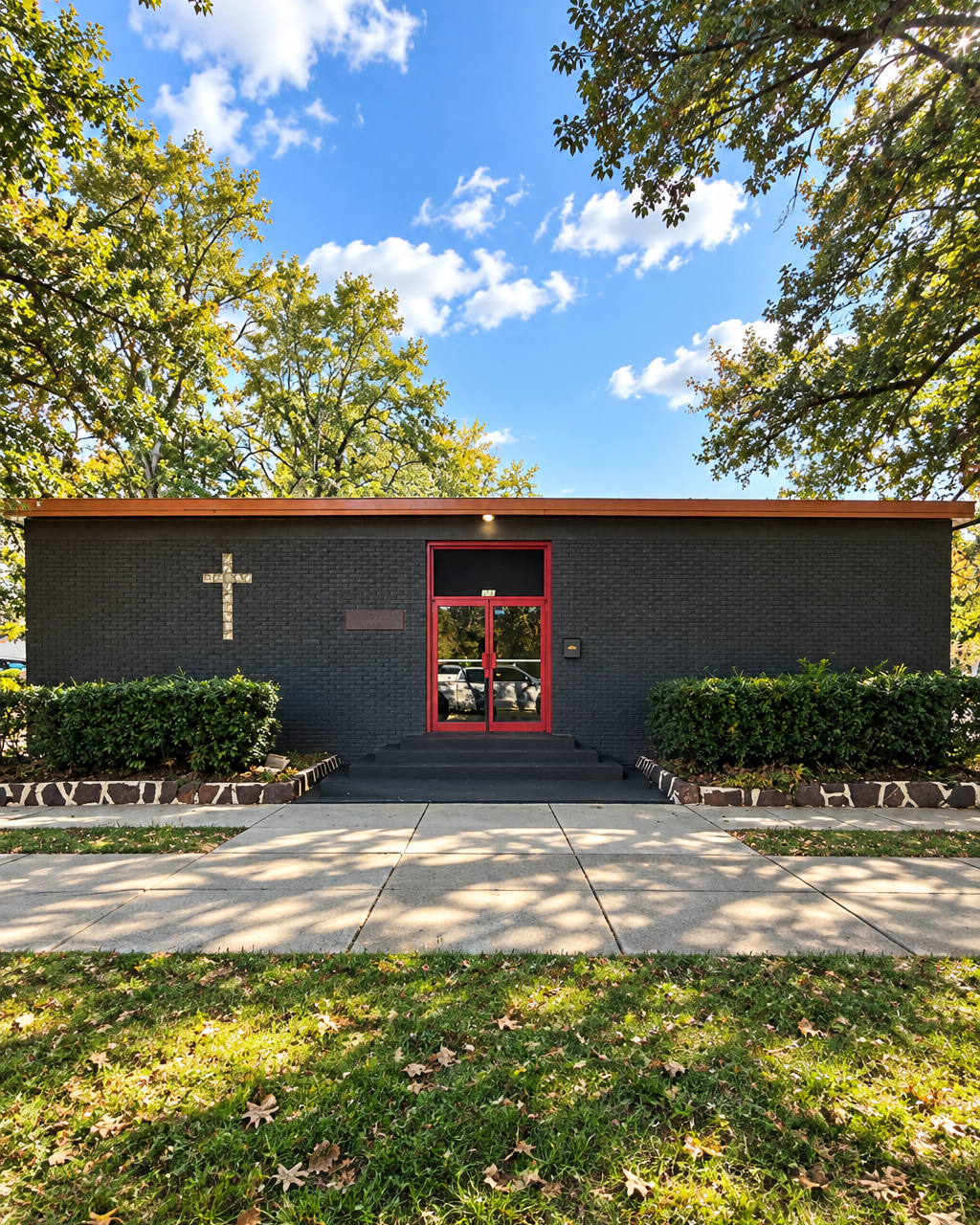 The Reaching Out CDC church building in Mobile, Alabama — dark brick exterior with a light cross on the wall and red-framed glass doors at the entrance